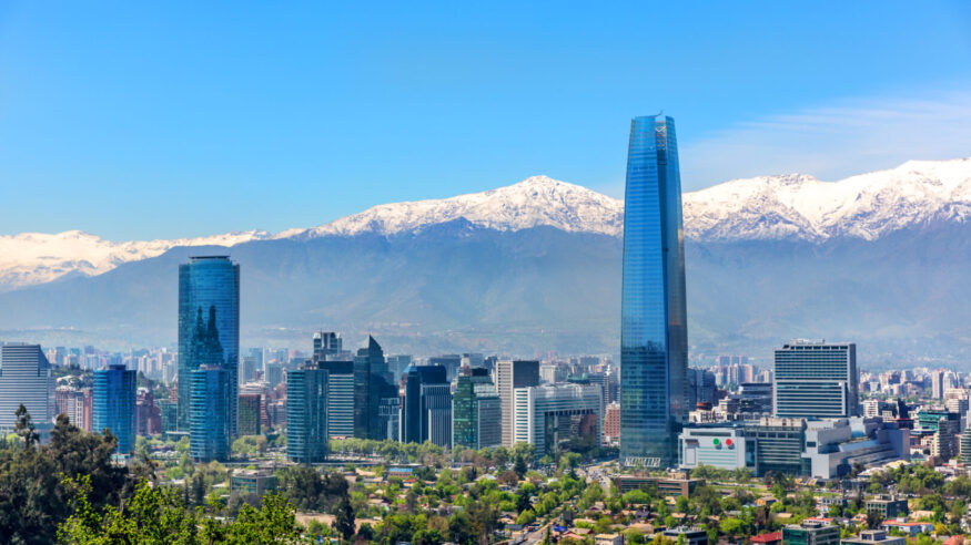 Plenty of business buildings in Santiago del Chile with trees in the foreground and the Andes mountains in the background