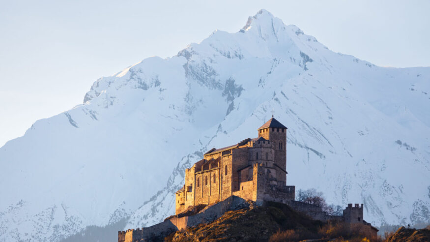 Winter landscape view of the Valere Basilica illuminated at golden hour in front of a snowy mountain, shot in Sion Wallis Switzerland